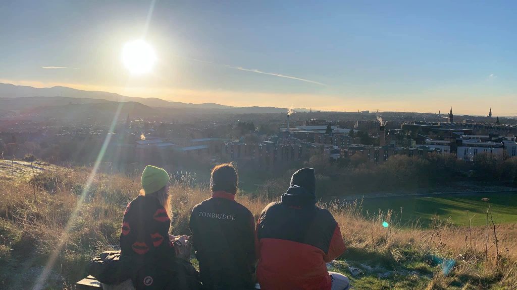 Three students enjoy the sunset from the top of Arthur's Seat.