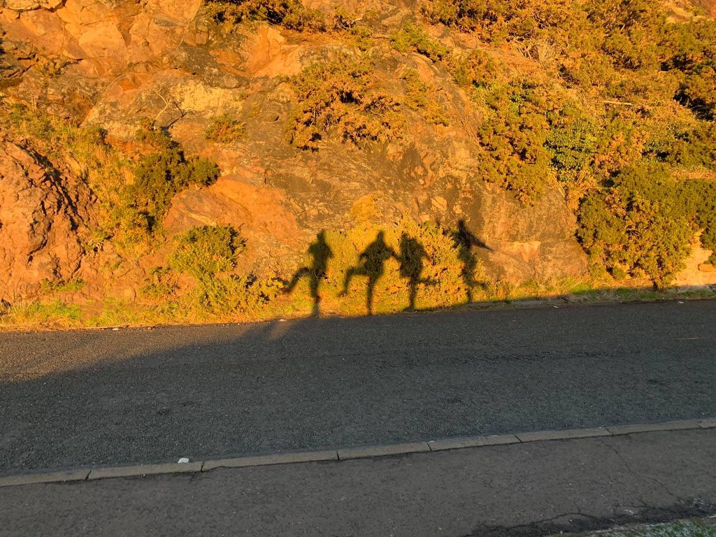 Four students' shadows as they walk up arthurs seat.