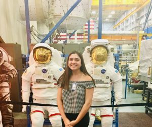 Mia is pictured in front of a museum exhibit of two life-sized NASA astronauts. She is wearing a badge that reads "VIP".