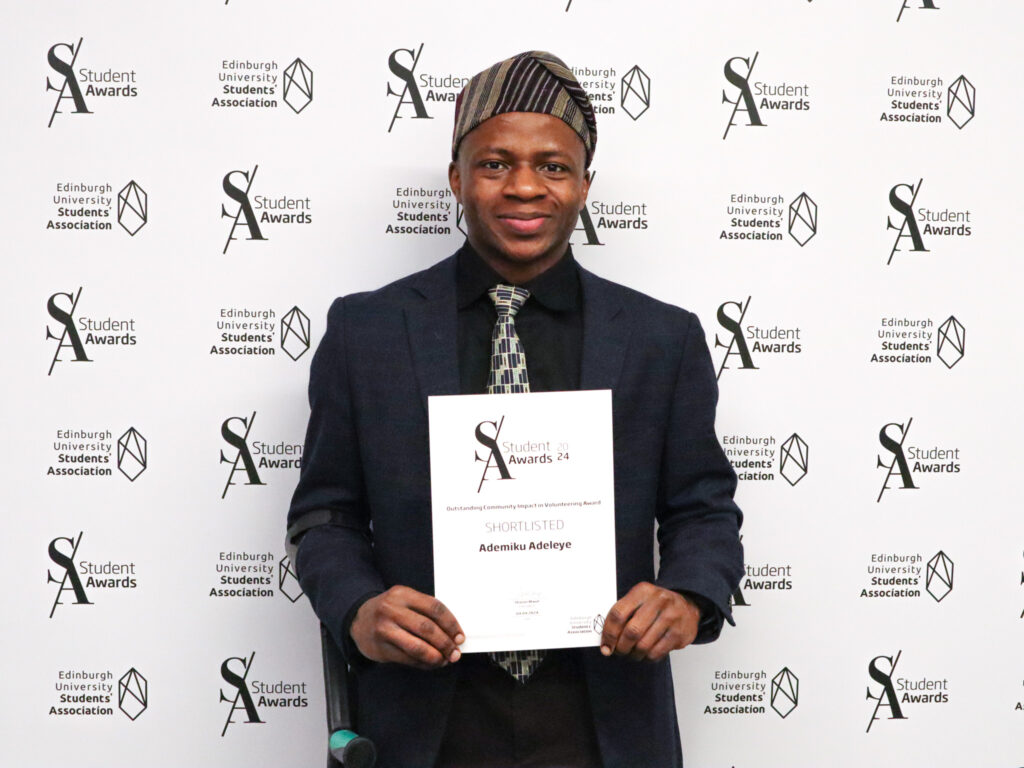 Photograph of Ademiku holding his award certificate