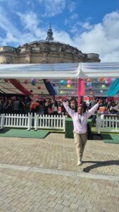 Jeannette poses with her arms raised in front of the Welcome Week tent at Bristo Square. 
