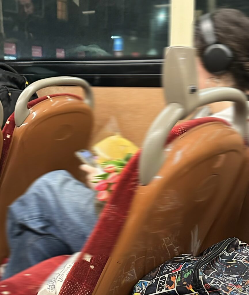 A person is captured sitting on a bus. The image is slightly blurry but they can be seen holding a bouquet of flowers.
