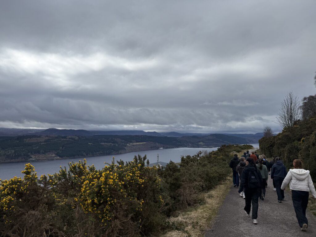 A group of people are pictured walking down a path on a hill, next to a lake.