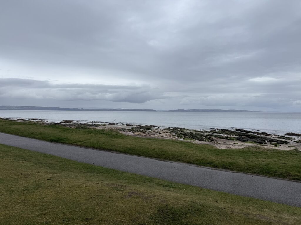 A view of the beach in Nairn, with a patch of grass and a path in the foreground