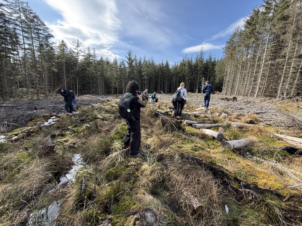 A group of students standing in an open field surrounded by trees, preparing to plant more