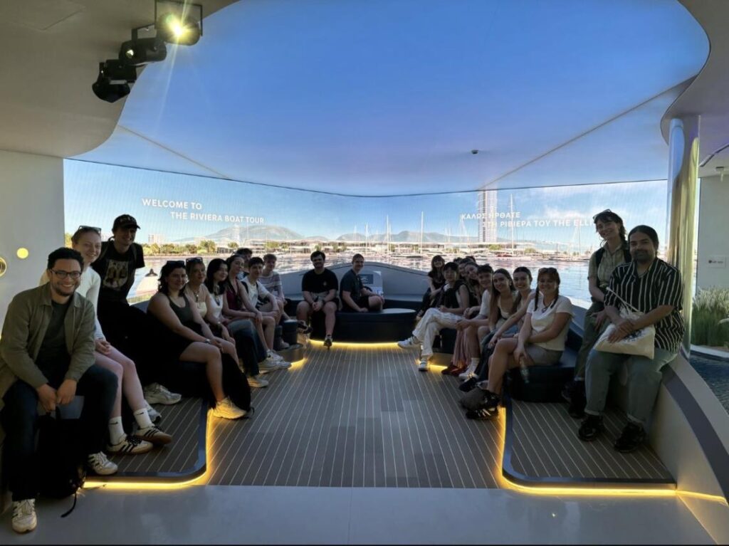 The Geography cohort on their Athens field trip are pictured sitting on a model boat, and smiling for the camera.