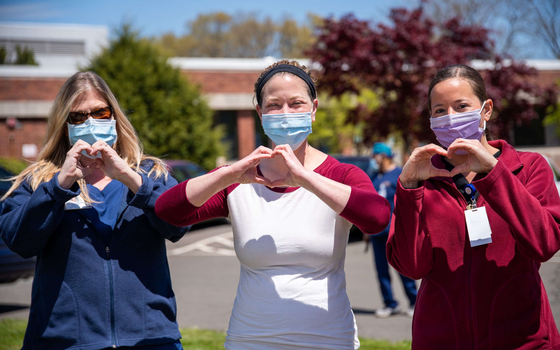 Three women wearing masks and making heart shapes with their hands