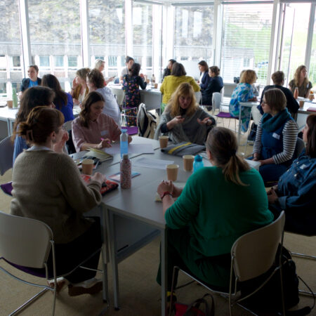Groups of people sit talking around tables in a light filled room