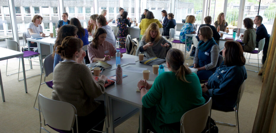 Groups of people sit talking around tables in a light filled room
