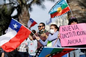 Protestors waving the Chilean flag and holding signs that read 'nueva constitutión ahora!!!'