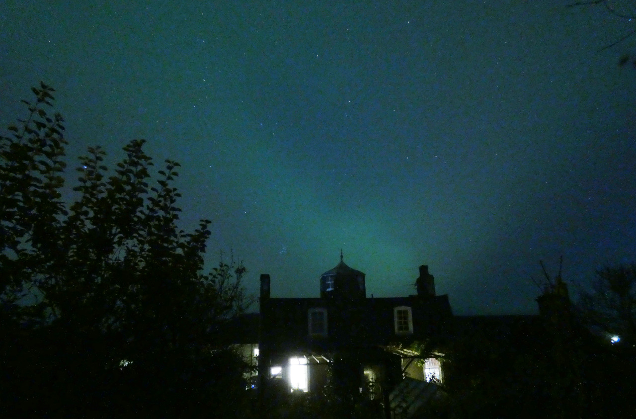 Green glowing night sky with silhouette house and tree in foreground