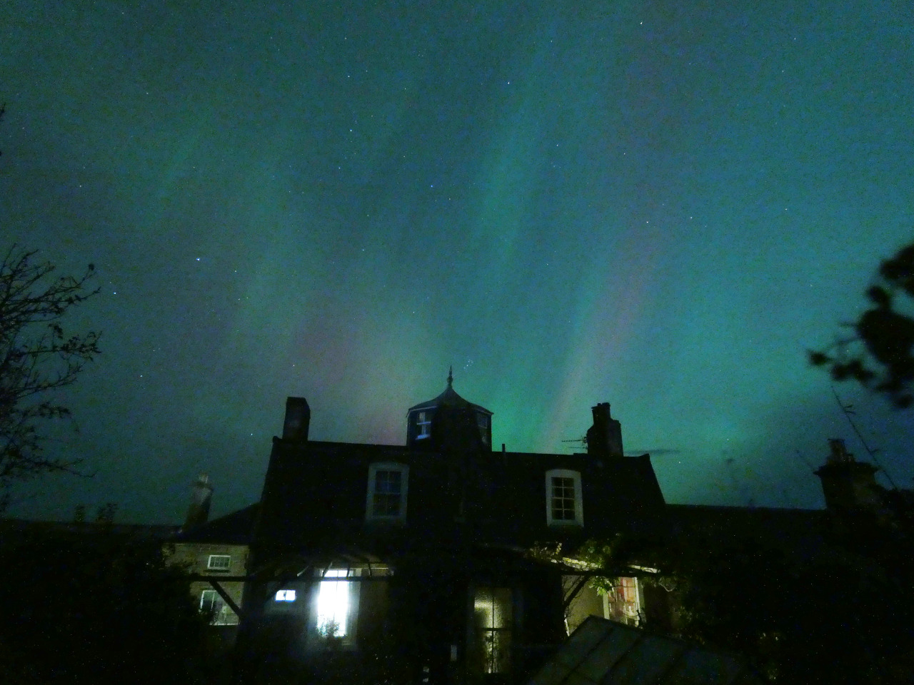 glowing pink and green night sky with silhouette house in foreground