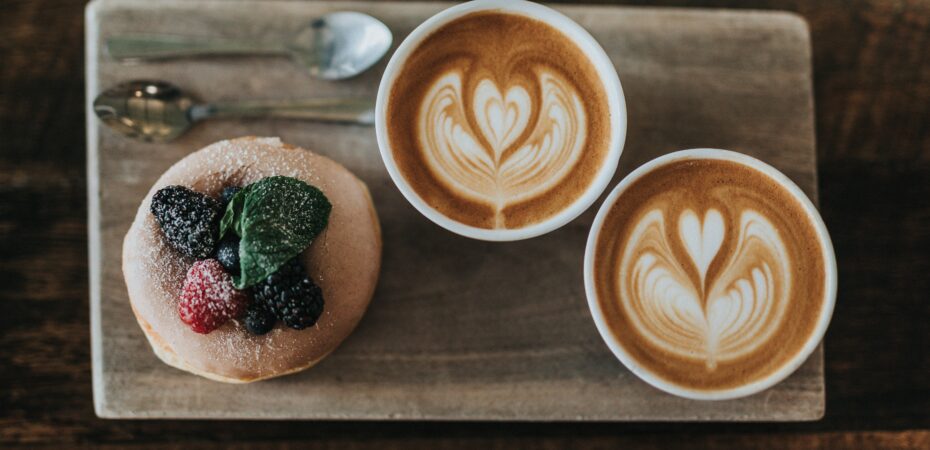 2 cappuccini and a fruit muffin on a wooden board