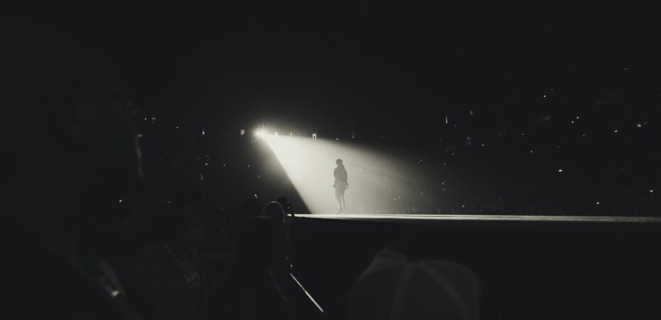 Black and white photo of someone on a stage in spotlight.