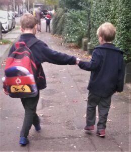 Back view of two children in school uniform walking to school together. A father and child walk together up ahead.