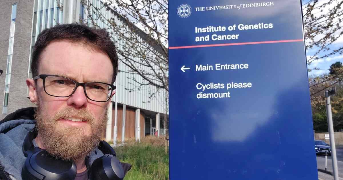 Filip standing by the Institute of Genetics and Cancer sign