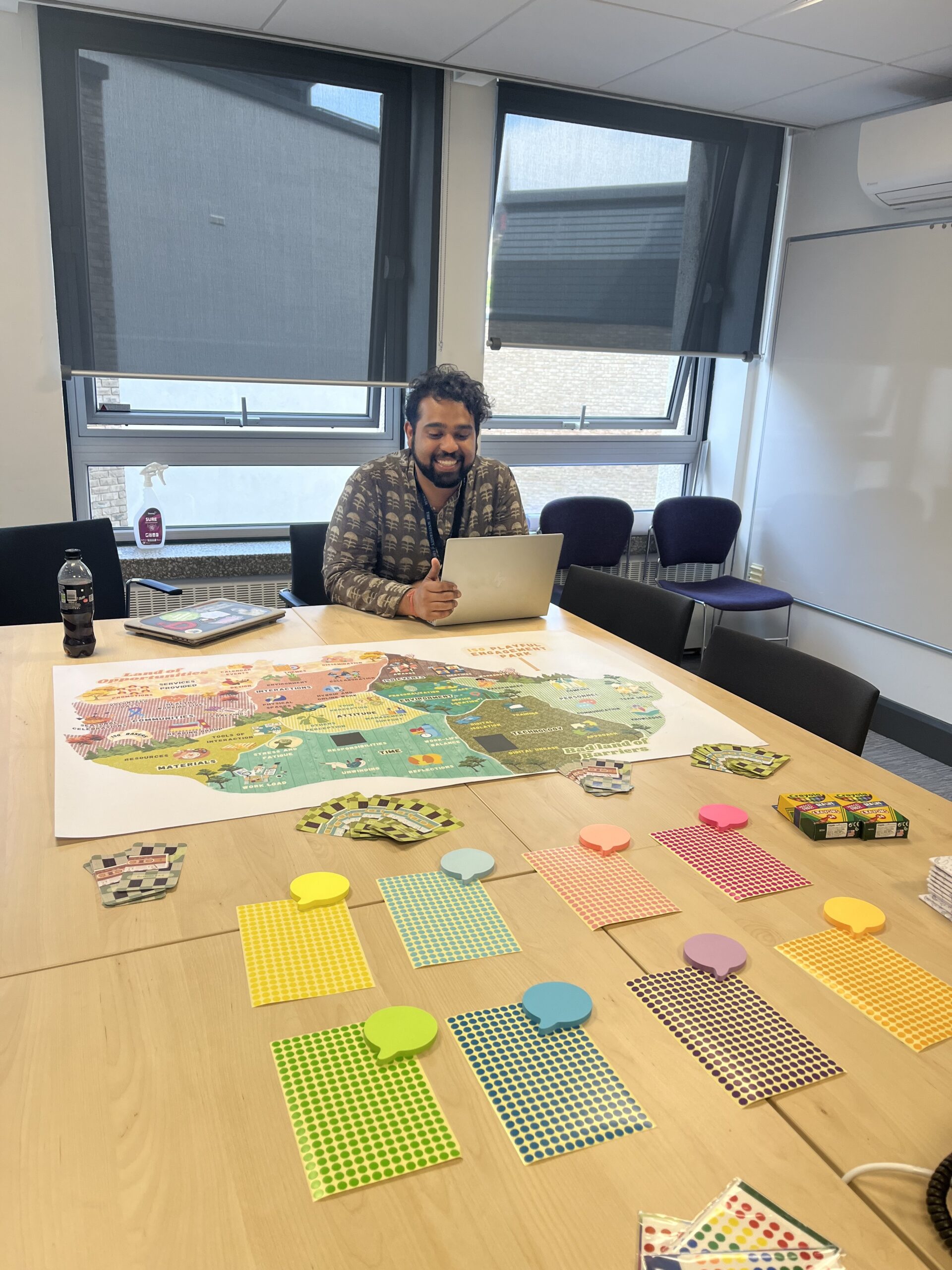 Ayaan Ahmed smiling next to a table with the map, post it notes, and stickers used in the focus group.