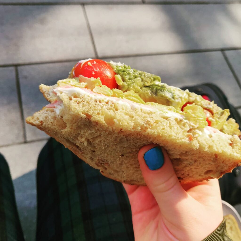 Avocado and tomato sandwhich, held by person's hand.