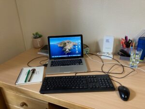 Laptop on desk with a notebook and other personal belongings. 