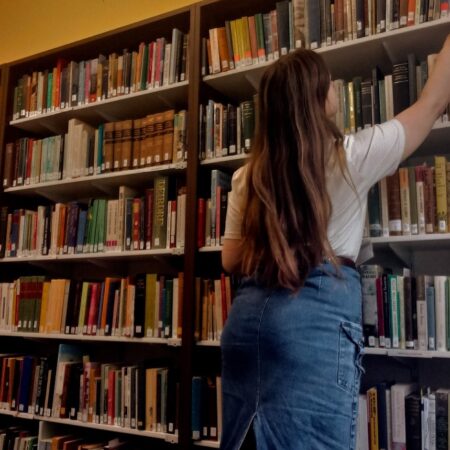 Ailsa, a girl in a blue denim skirt and white T shirt, reaches up to get a book from a shelf