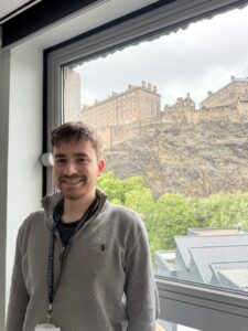 Intern Reuben stands in front of the view of Edinburgh Castle from Argyle House