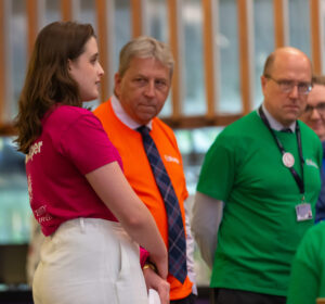 Leah wearing an EdHelp shirt in the Main Library. Two people with EdHelp shirts stand to her right further away from the camera.