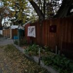 A back alley in the fall with a garden and a few pictures hung on the fence. 