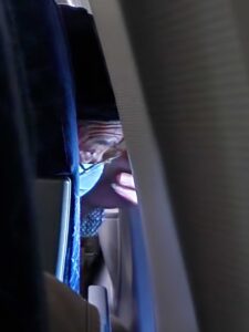 Masked man sneaking a peak out an airplane window
