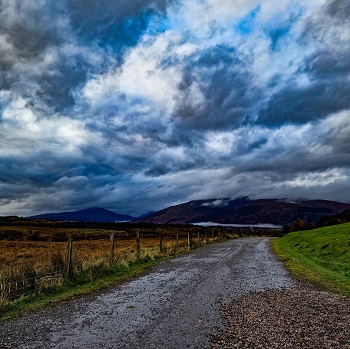 cloudy skies above a hill and lane in the countryside