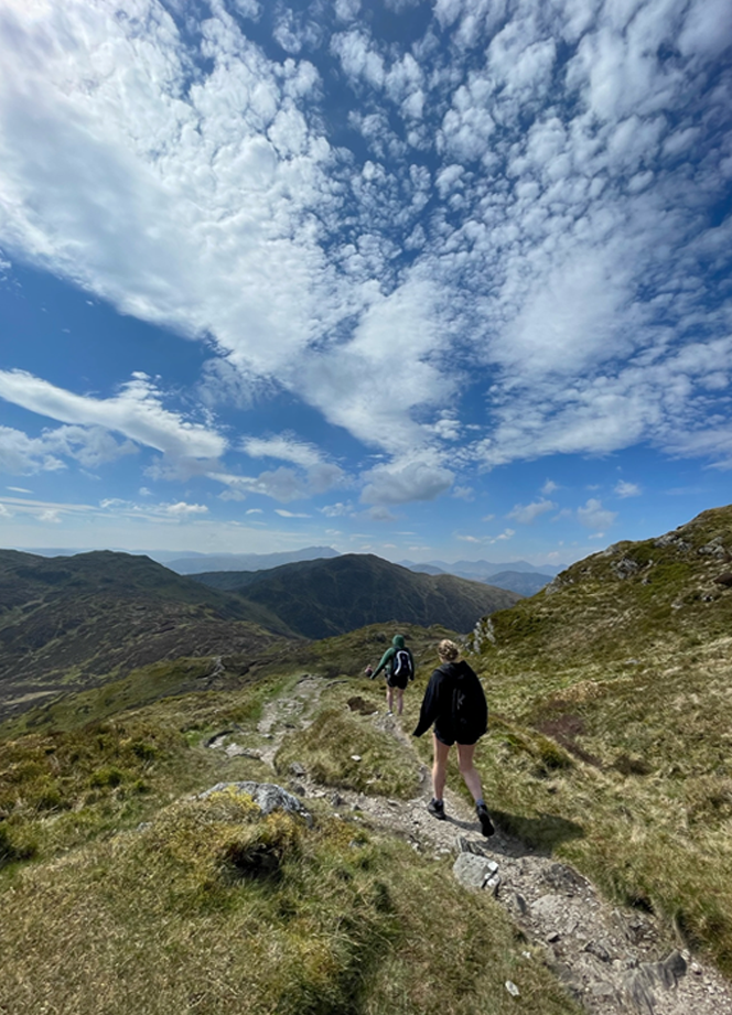 Walkers hiking on a trail, with a dramatic sky.