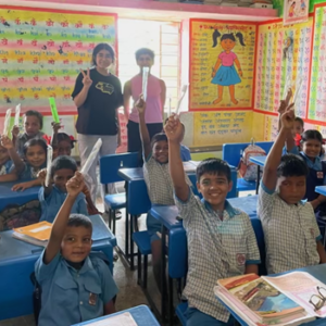 Saloni with school teacher in classroom of school pupils holding up their toothbrushes in the air.