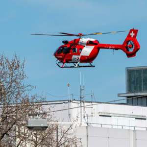 Red air ambulance landing over hospital building.