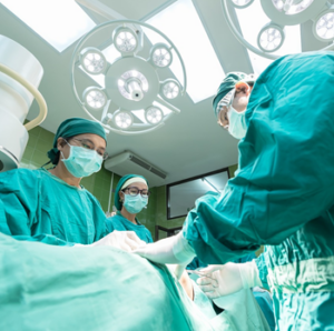 Three surgeons in green scrubs operating on a patient in the operating theatre.