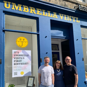 The owners of Umbrella Vinyl standing outside the shop with the shop door and signage in the background.