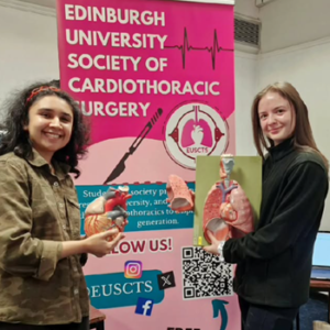 Two medical students standing in front of Edinburgh University Society of Cardiothoracic Surgery (EUSCTS) banner