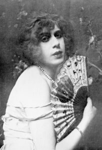 Black and white image of lili ebe holding a fan to her face 