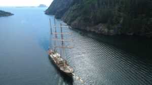image of tall ship from a birds eye angle with view of whole ship in ocean sailing past mountain