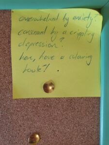 A yellow postit note tacked to a board, with cursive script in blue.
