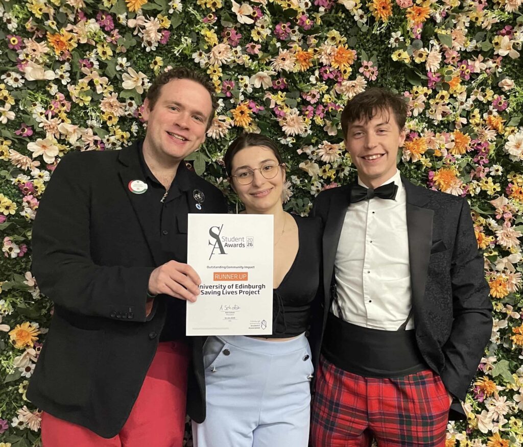 Students collect their award certificate against a floral backdrop.