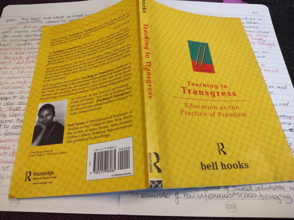 A yellow book likes face down - the front cover says "Teaching to Transgress: Education as the Practice of Freedom. bell hooks. Routledge. The back of the book has a lot of text and a photo of bell hooks