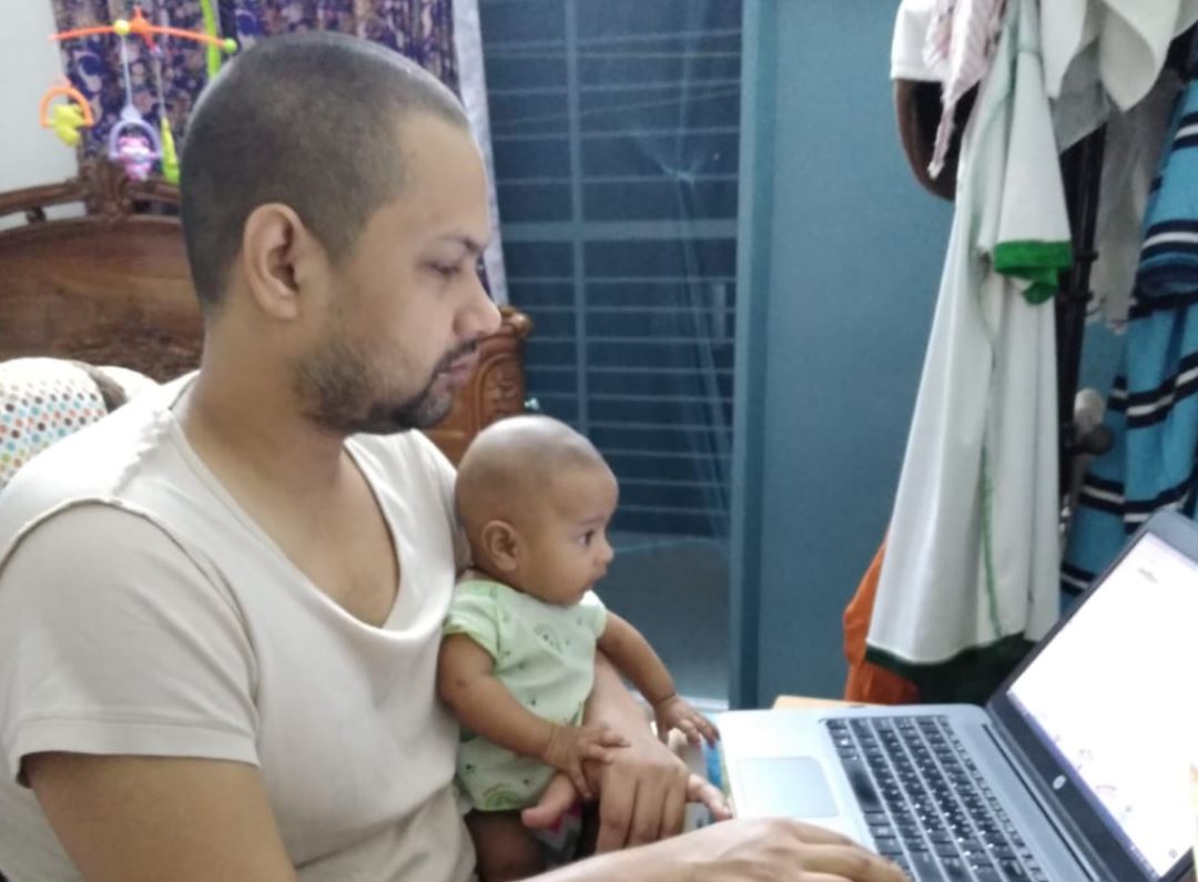 Monjurul holding his baby while studying on laptop