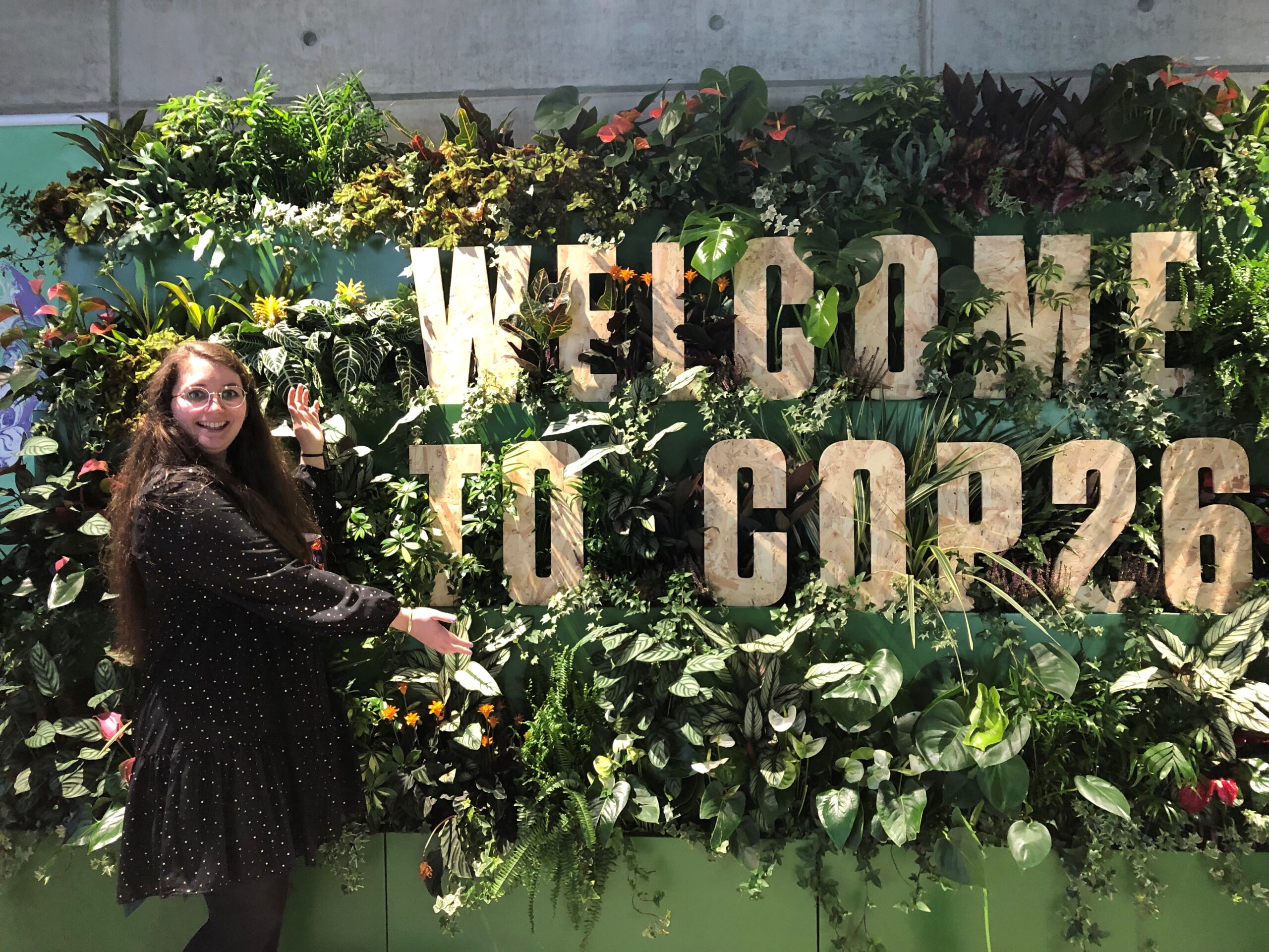 Kirsten Leggatt next to a sign saying "Welcome to COP26"