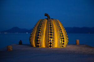 A sculpture in the shape of a pumpkin, the fruit part is yellow with black polka dots on it, and the tip part is black with small yellow polka dots on it.