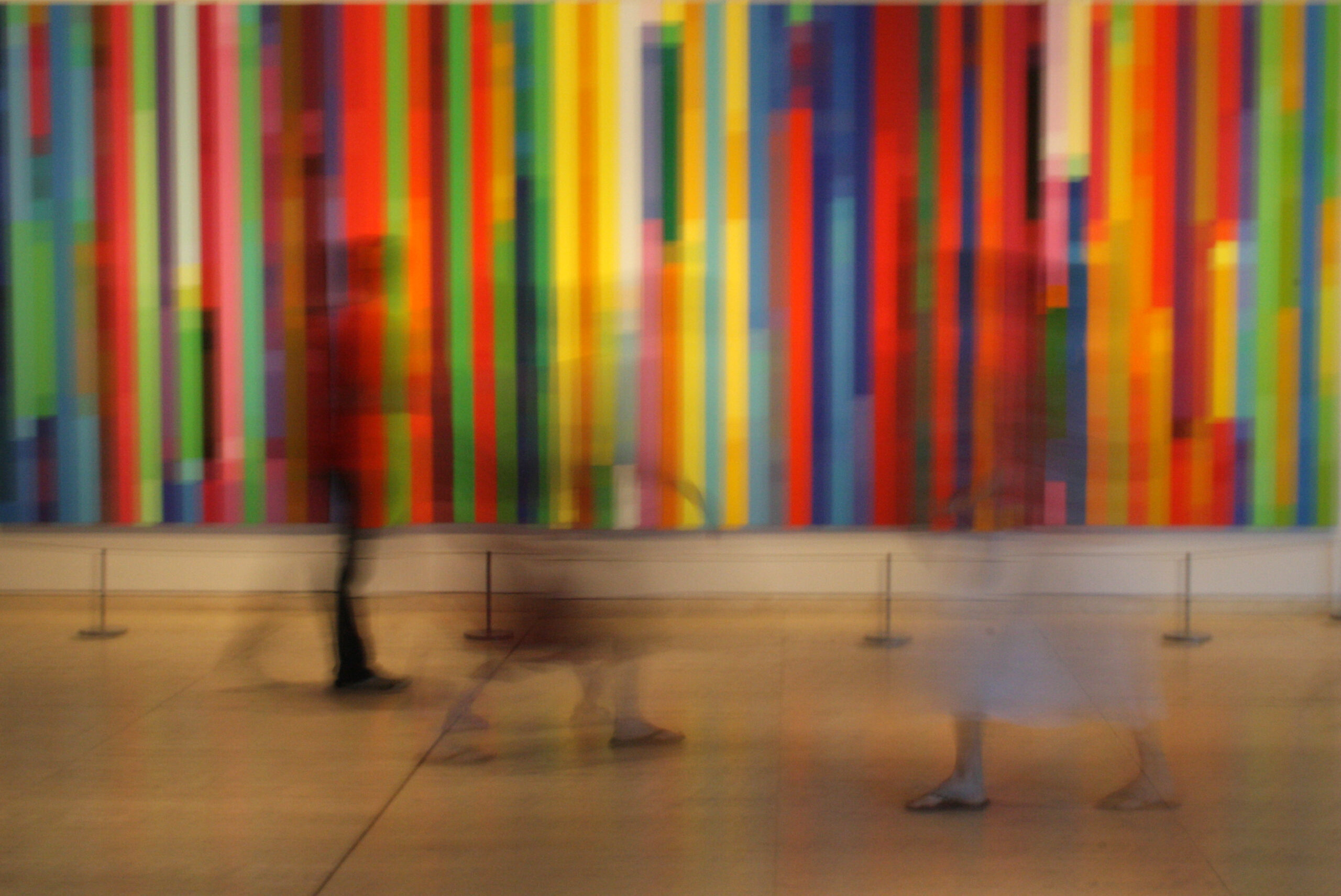 This is a colorful, time-lapse photo. The background is colored lines, and the foreground is a blur of moving figures.