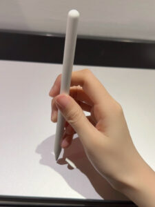 Soft Pen Grip Position. One hand holds the pen vertically, with the thumb and forefinger tips pinched tightly together, the middle finger under the forefinger, and the rest of the fingers together under the barrel for support. and the wrist hangs slightly.