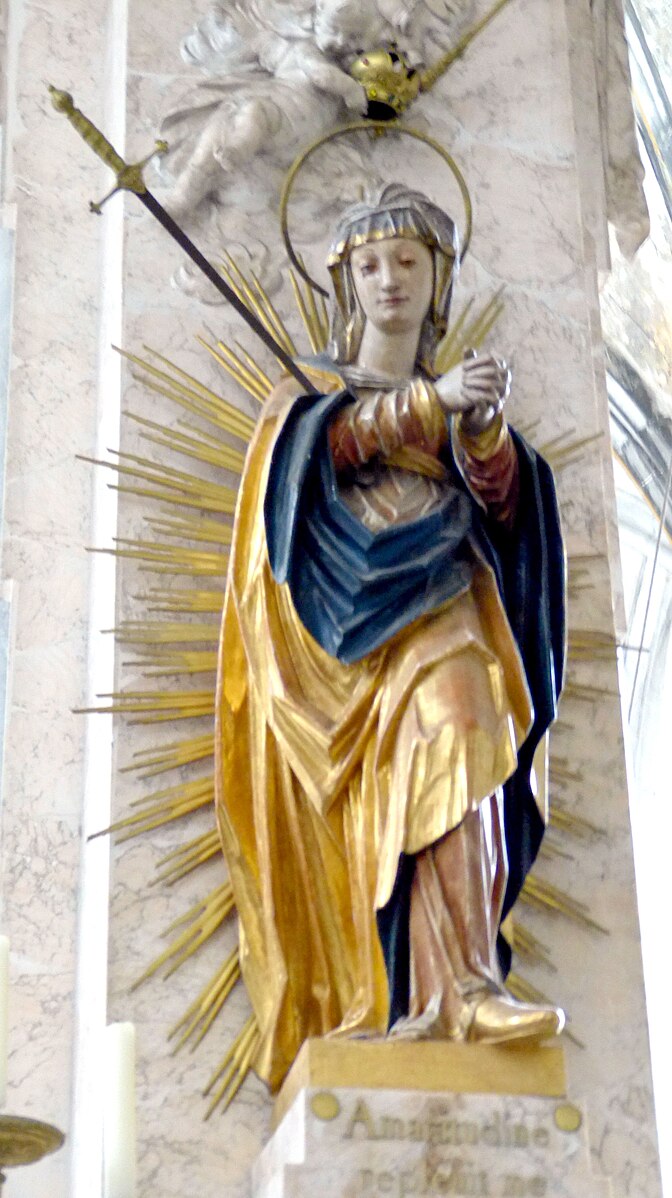 Statue of a robed Virgin Mary impaled with a sword. She has a halo and golden rays are omitted from her figure.