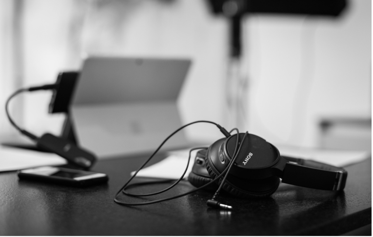 A pair of Sony headphones, a smartphone, and a tablet on a dark desk in black and white.