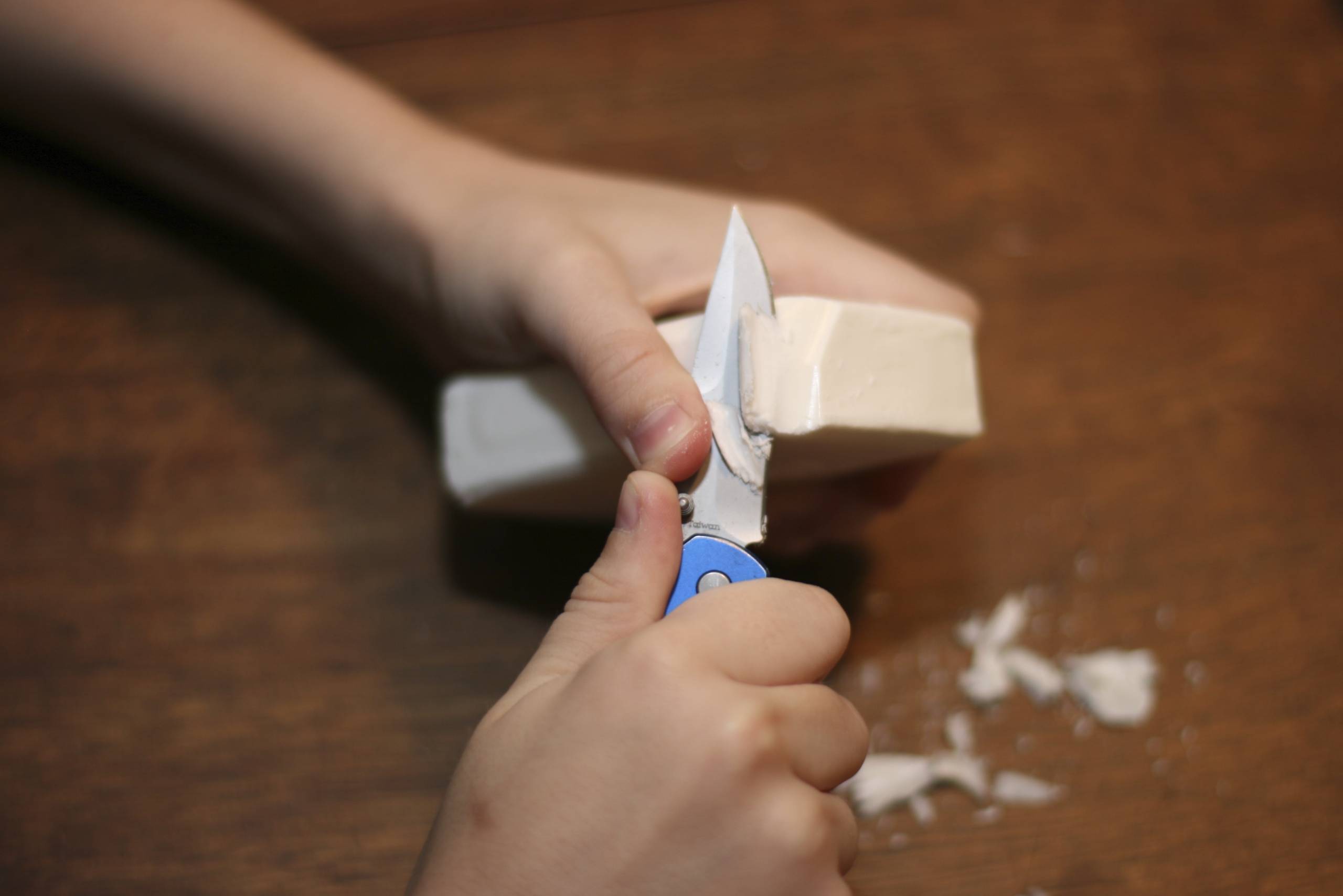 A hand uses a small knife to carve an object.