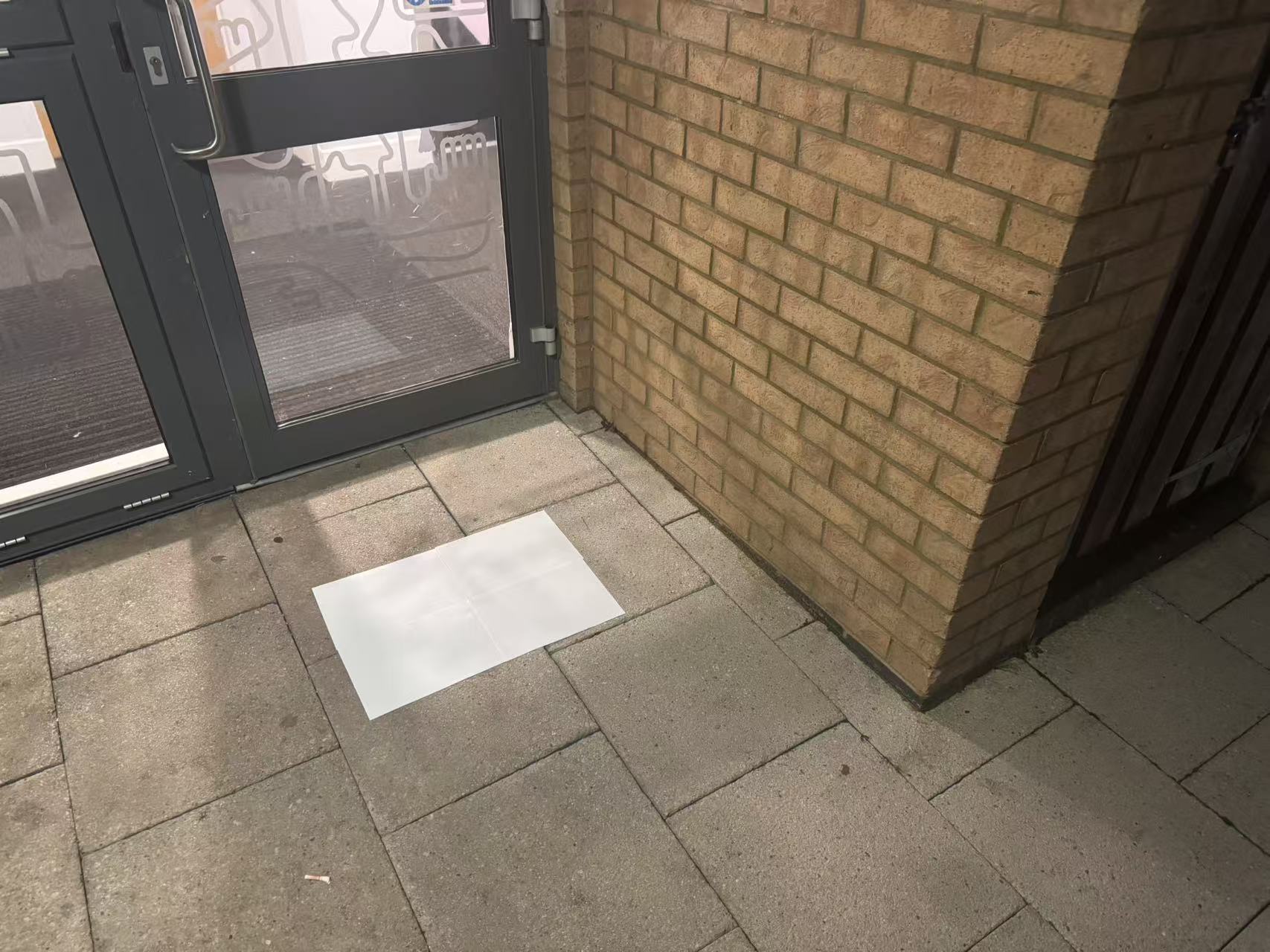 The scene is at the entrance of a building, with four white sheets of paper placed on the ground outside the gate.