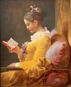 A young woman in a yellow dress sits sideways in a chair and reads a book. ________________
